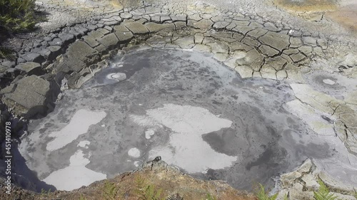 Valley of Geysers, Kamchatka. The mud cauldron is filled with a gray boiling liquid. On the surface, the bubbles swell and burst. The clay on the dry edges is cracked. A sunny day
