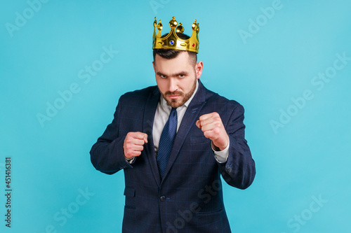 Photography Young adult businessman wearing official style suit and golden crown, punching to camera, provoking fight or ready to self-defense, struggle concept
