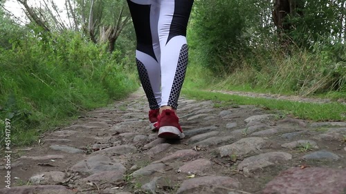 Legs of a girl in sports leggings are walking along the road. Road with stones photo