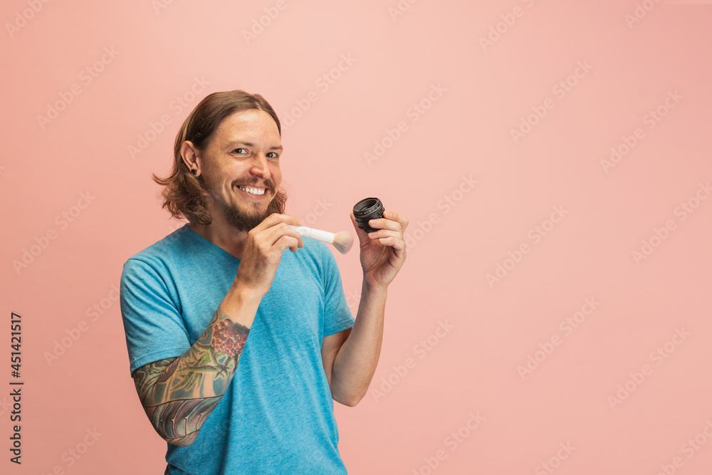 Portrait of young man, photographer, cameraman with camera lens having fun isolated on pink studio background. Concept of occupation, job, funny meme emotions