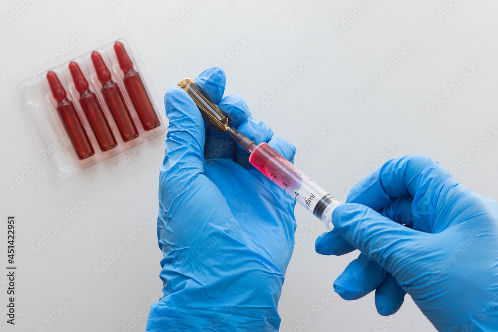 Top view of woman hands in medical gloves filling syringe barrel with vitamin group B for injection Top view of woman hands in medical gloves filling syringe barrel with vitamin group B for injection