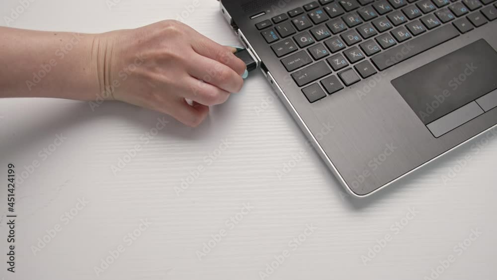 female hands connected a USB flash drive to a computer on a light background, close-up female hands connected a USB flash drive to a computer on a light background, close-up