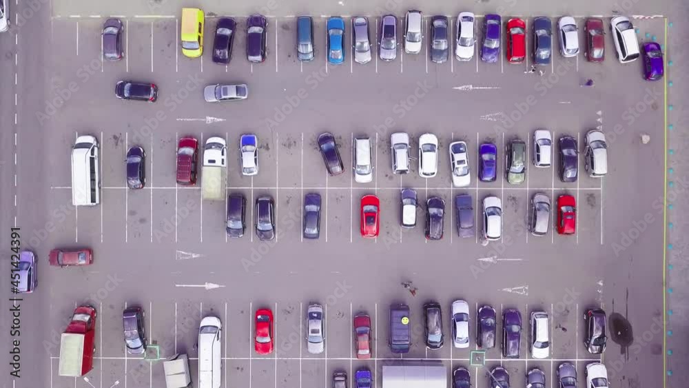 A bird's-eye view of parked cars in the parking lot near the shopping center. The camera is directed vertically downwards. Parking of cars in the open air. Summer. A bird's-eye view of parked cars in the parking lot near the shopping center. The camera is directed vertically downwards. Parking of cars in the open air. Summer.