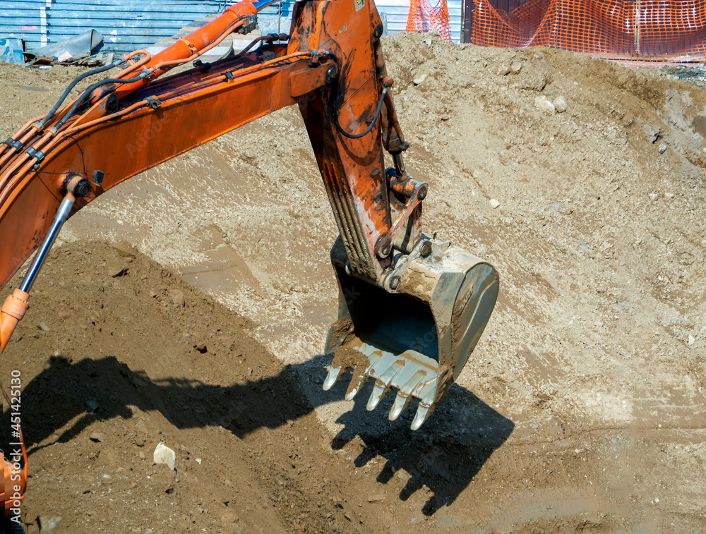 Fototapeta premium The excavator bucket is lowered into the pit to pick up the soil from there. Close-up. Background with a construction site for industry and business.