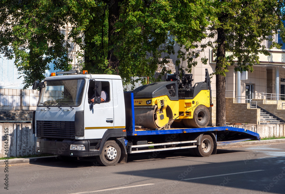 A tow truck transports the road roller on a stationary platform to the place of work. Background for business and industry. A tow truck transports the road roller on a stationary platform to the place of work. Background for business and industry.