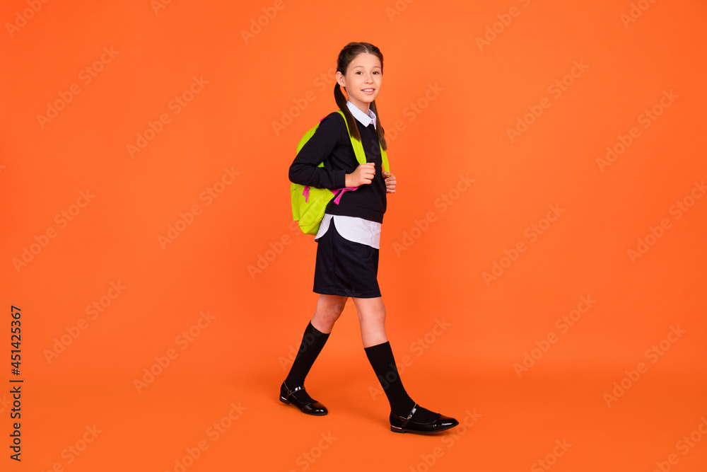 Full length photo of pretty cute small schoolgirl go school wear backpack isolated on orange color background
