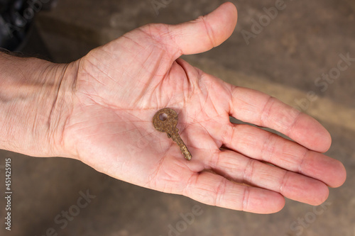 Old rusty key in hand. Vintage key in open hand palm. Owner holding house key. Security and safety concept. Aged iron key in man's arm. House protection concept.