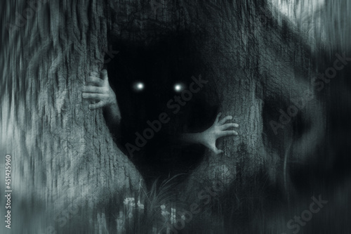 A spooky horror concept of a monster with glowing eyes, hiding in a tree trunk, in a dark spooky forest. With a grunge, blurred, edit.