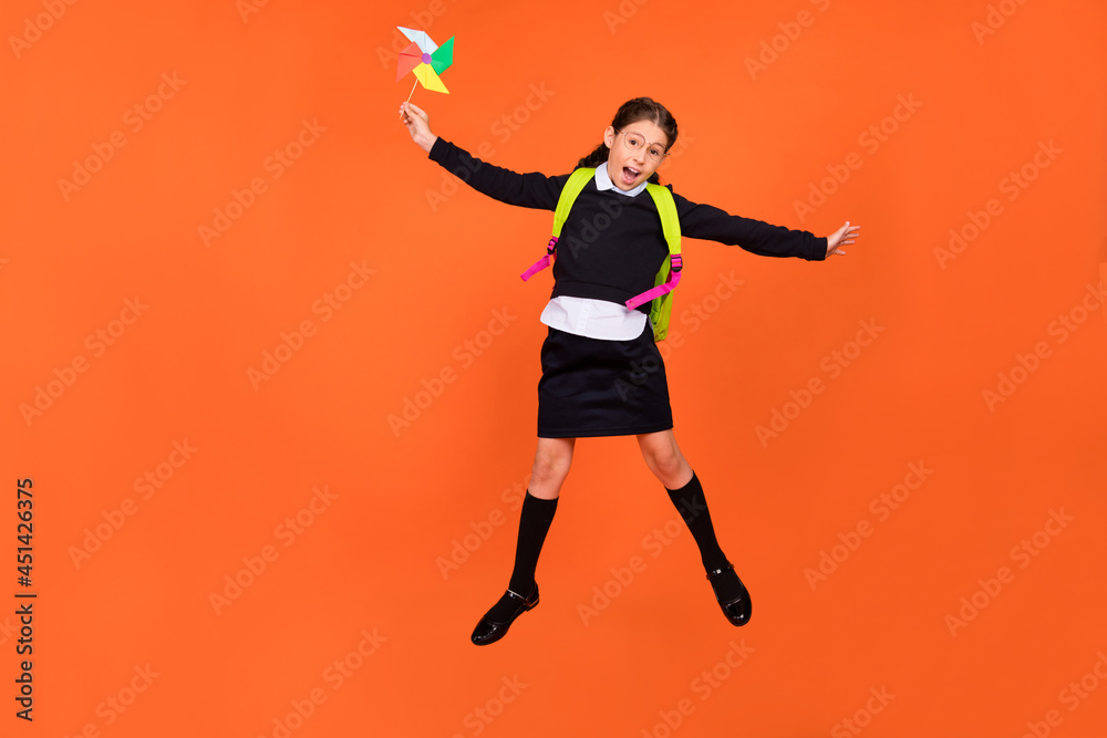Photo of energetic schoolgirl jump hold propeller toy wear uniform rucksack isolated orange color background