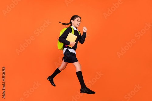 Profile photo of active schoolgirl jump hold book run wear uniform backpack isolated orange color background