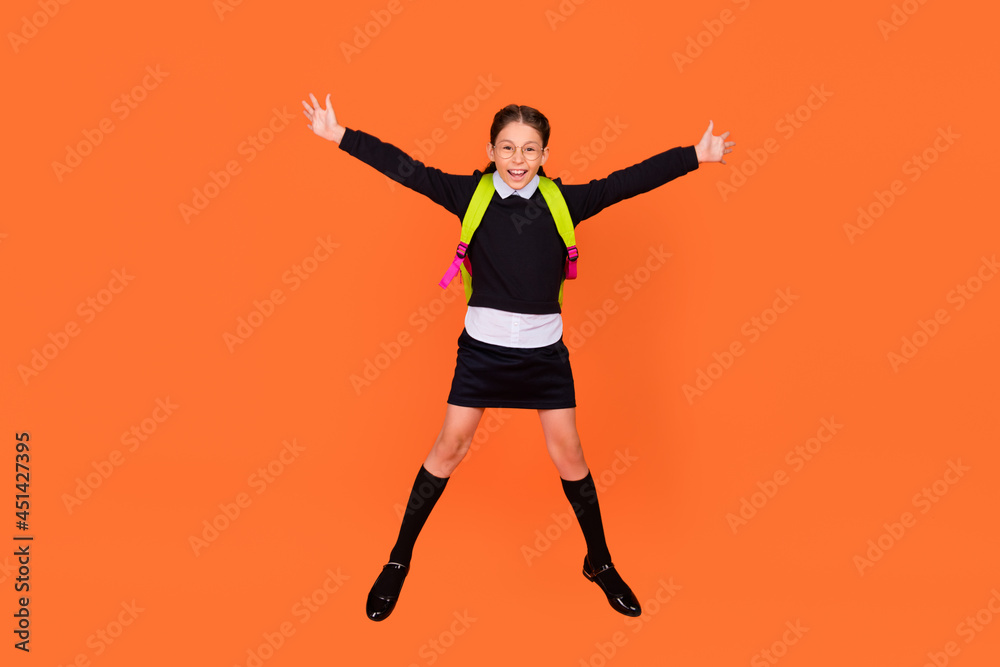 Full length photo of cheerful happy schoolgirl jump up wear backpack glasses isolated on orange color background