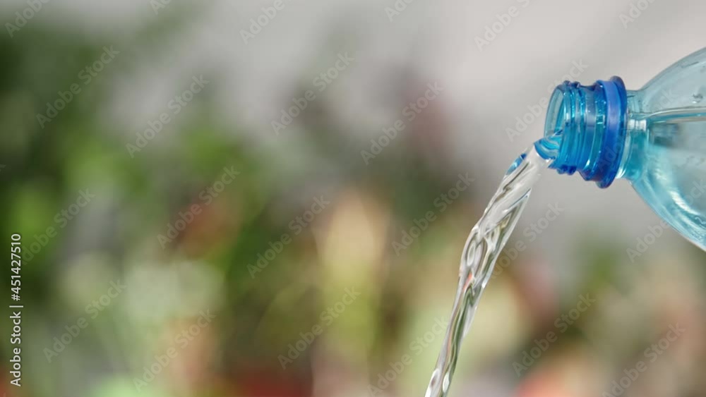 clean cool water is pouring a plastic with a transparent blue bottle on a green background, close-up clean cool water is pouring a plastic with a transparent blue bottle on a green background, close-up