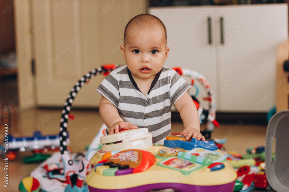 Cute chubby baby stands and plays with a children's music table. Lots of colorful toys everywhere. Cute chubby baby stands and plays with a children's music table. Lots of colorful toys everywhere.
