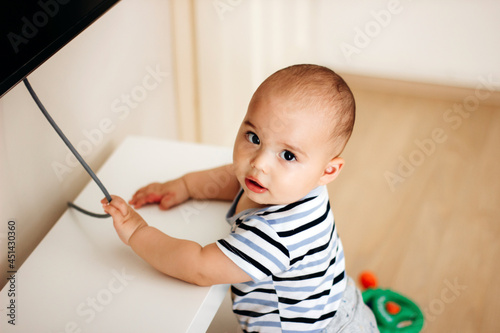 Sweet naughty baby boy pulls the electric cord from the TV