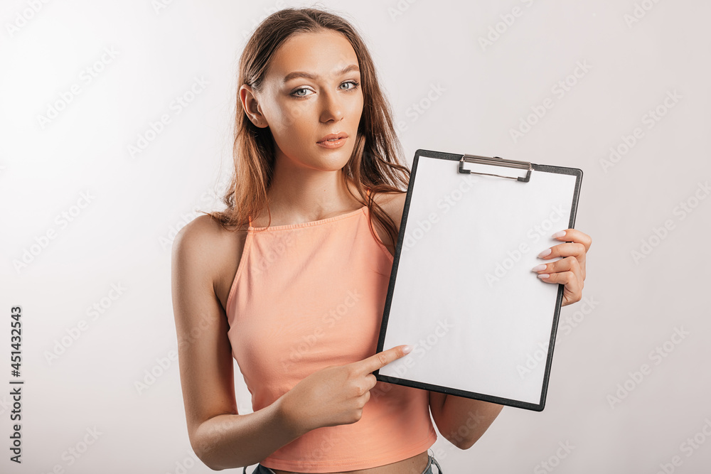 Girl student points to the sheet. Beautiful young business woman holds a clipboard with mockup blank space isolated on gray background. Study and business concept. Online learning cover Girl student points to the sheet. Beautiful young business woman holds a clipboard with mockup blank space isolated on gray background. Study and business concept. Online learning cover