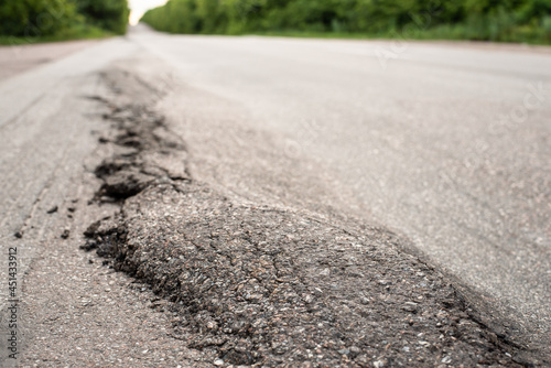 Close-up photo of damaged road in the countryside. Asphalt surface crushed and ran down due to heavy trucks driving. Problem of overloaded trucks
