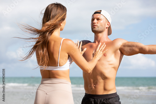 young man stretching and exercising outdoors from trainer suggesting on the beach