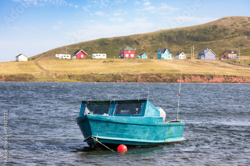Small blue boat moored in the blue waters of the Magdalen Islands. Colourful wooden houses line the coastline behind. Canada. photo