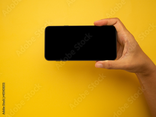 Hand holding of a smartphone with a yellow background. Close-up photo. Space for text. Technology and communication concept