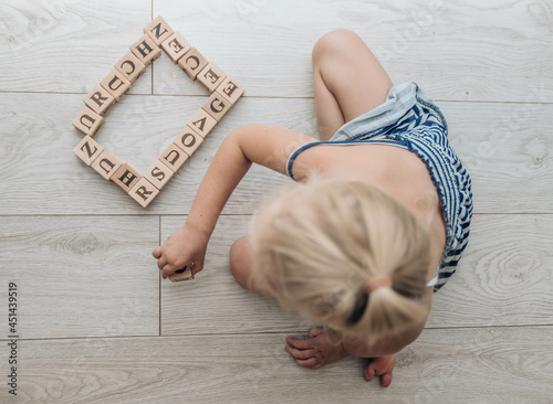 Little girl playing and educating with abc cubes indoors. Little girl child  playing with wooden blocks on the floor