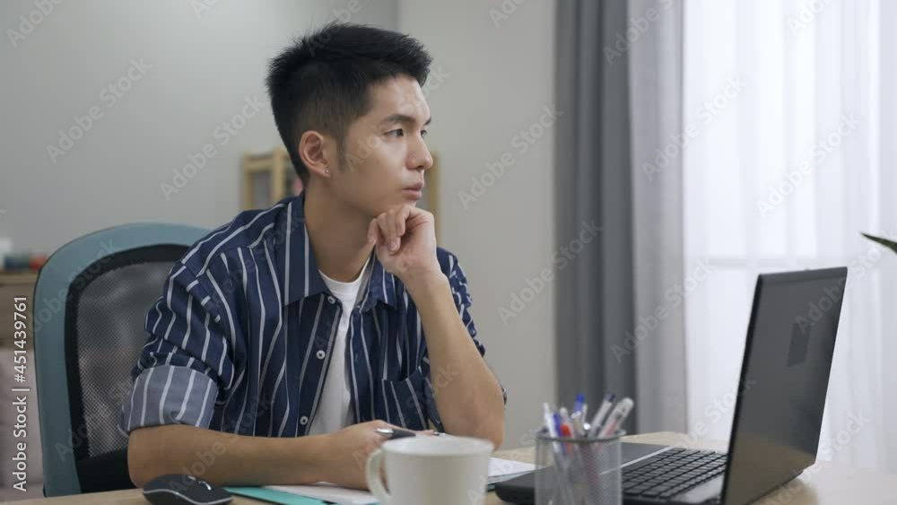 handsome asian creative worker sitting still at desk is spinning pen with his hand under chin while gazing into the space in contemplation at home. handsome asian creative worker sitting still at desk is spinning pen with his hand under chin while gazing into the space in contemplation at home.