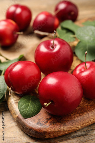 Delicious ripe cherry plums with leaves on wooden table, closeup