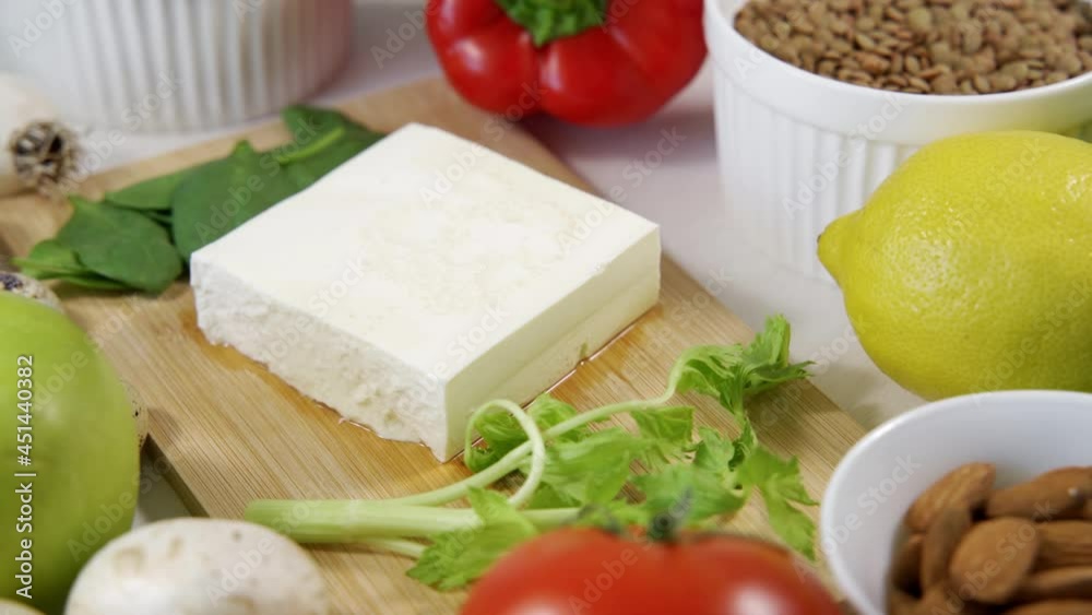 A piece of feta cheese lies on a wooden cutting board, surrounded by many vegetables and quail eggs. Close-up, top view, the camera rotates. A piece of feta cheese lies on a wooden cutting board, surrounded by many vegetables and quail eggs. Close-up, top view, the camera rotates.