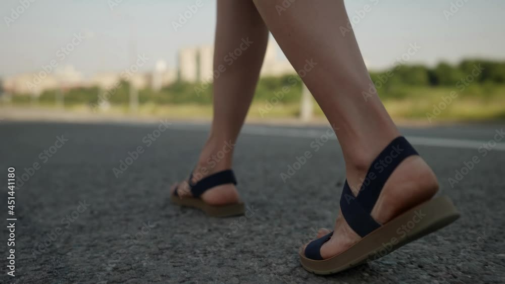 woman is walking on asphalt road in city, closeup of female feet in sandals woman is walking on asphalt road in city, closeup of female feet in sandals