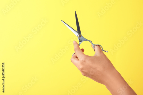 Hairdresser holding professional scissors and space for text on yellow background  closeup. Haircut tool