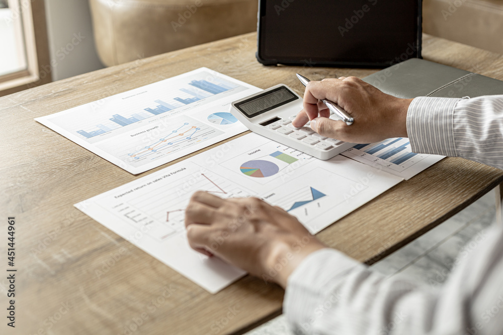 A financial scholar is looking at a financial document to verify the accuracy of a company's financial data, he is pressing a white calculator, a line chart and a pie chart. Finance concept. A financial scholar is looking at a financial document to verify the accuracy of a company's financial data, he is pressing a white calculator, a line chart and a pie chart. Finance concept.