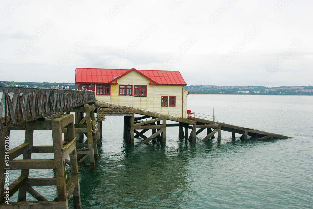 An old lifeboat station in old pier South Wales, Swansea. White station with red roof and ramp for boat.