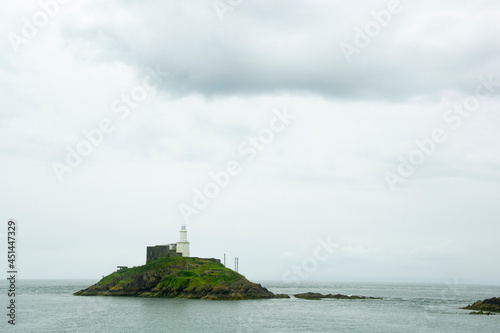 An old white lighthouse in the sea on green rocky hills, South Wales, UK
