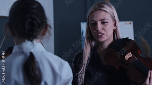 Young blonde woman teacher showing how to play violin to little girl student