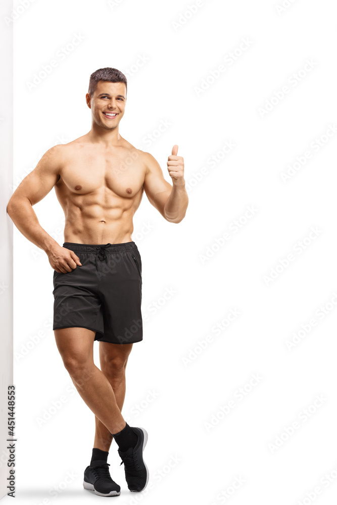 Full length portrait of a muscular man leaning shirtless on a wall and showing thumbs up Full length portrait of a muscular man leaning shirtless on a wall and showing thumbs up