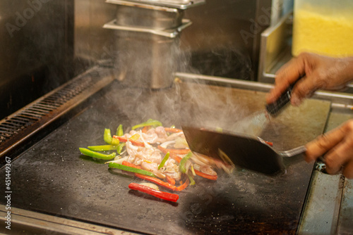Slika na platnu Mexican chef's hands preparing some chicken fajitas on a very hot restaurant gri