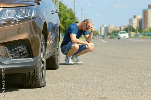 The man is upset sitting near the car, a tire puncture, a flat car wheel
