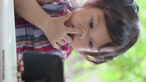 Close-up of an Asian girl staring at a smartphone on the dining table, the concept of a child addicted to the phone to distraction, the child is too addicted to cartoons and games, vertical video.