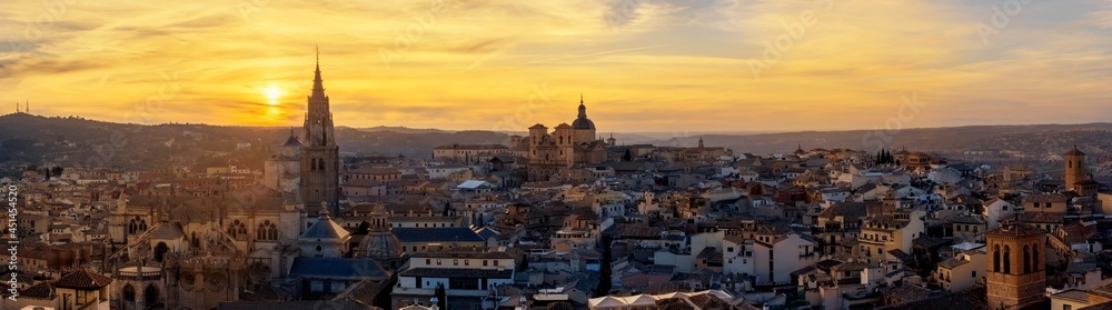 Panoramic view of skyline of old part of the city with small streets in a colorful sunset between the belfry of the tower of the old cathedral of Toledo in orange sunset, Spain.