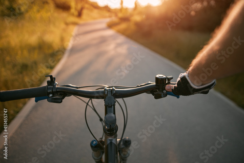 A man riding a bike. Holding bike handlebar with one hand in a sports glove with sunlight at the top. Concept of summertime outdoor leisure sport activity. First-person view bicycle riding.