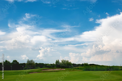 Beautiful green golf course with amazing blue sky, white clouds and distant trees background