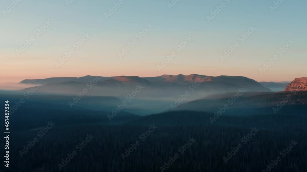 Beautiful left trucking aerial drone shot of the stunning wild Uinta Wasatch Cache National Forest in Utah with large pine trees below and stunning mountains covered in mist during a summer sunrise. Beautiful left trucking aerial drone shot of the stunning wild Uinta Wasatch Cache National Forest in Utah with large pine trees below and stunning mountains covered in mist during a summer sunrise.