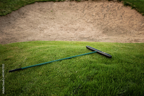 Golf course with a sand bunker, green grass and rake