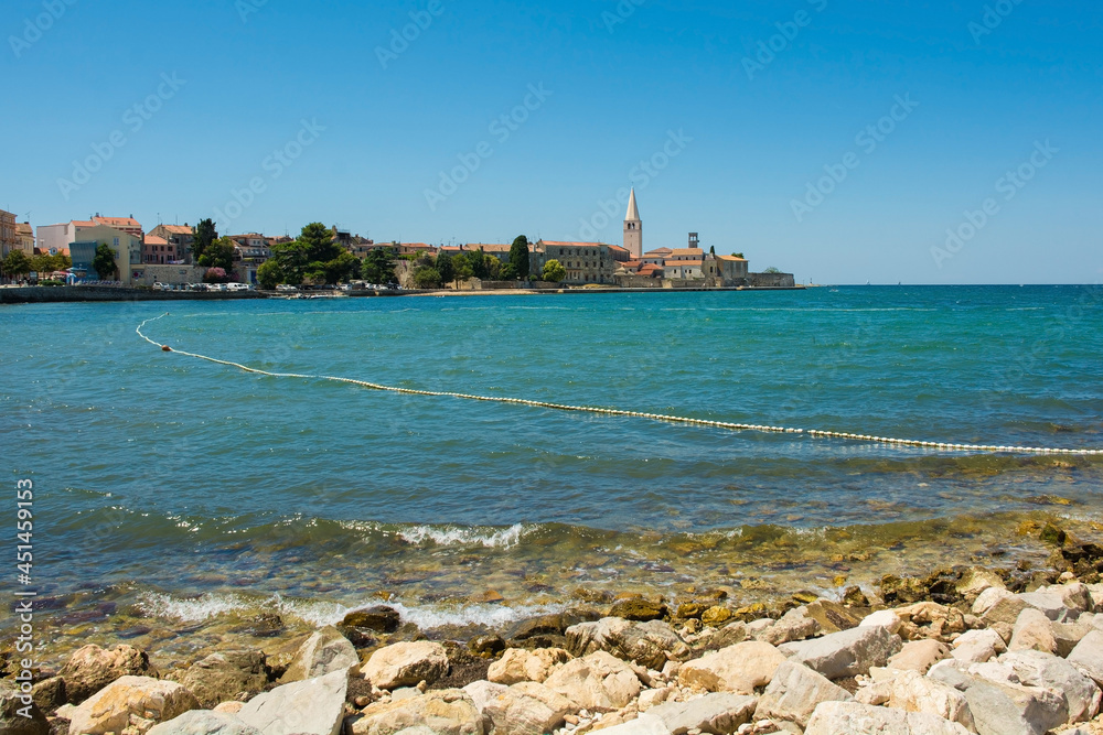 The historic medieval coastal town of Porec in Istria, Croatia, seen from the shore just north of the old town, with a swimming safety line in the water
