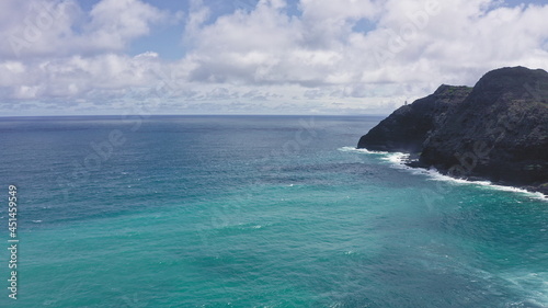 Flying drone over the ocean. View of makapuu lighthouse. Waves of Pacific Ocean wash Rocky shore. Magnificent mountains of Hawaiian island of Oahu against backdrop of blue sky with white clouds. photo