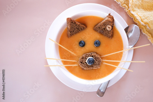 Fun food for kids - delicious, healthy and organic pumpkin or pea puree soup, garnished with corn and berries, a cat or fox face.
