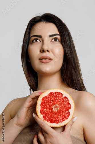 Portrait of a woman with perfect skin with natural make up hold grapefruit isolated on beige background studio portrait.