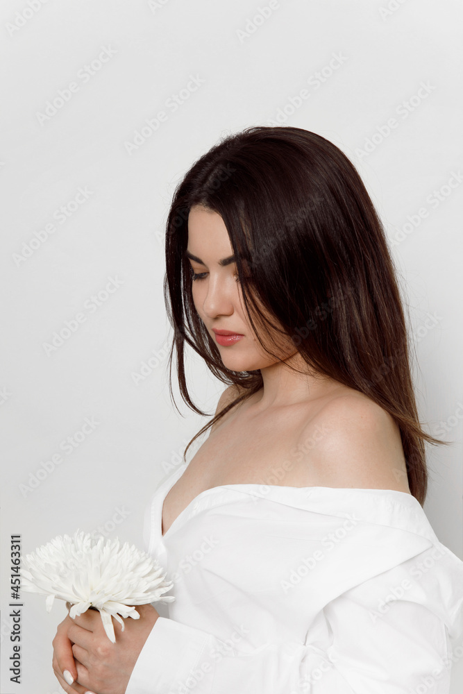 Beautiful sensual brunette young woman in a white t shirt holding a white flower, isolate on a white background. Beautiful sensual brunette young woman in a white t shirt holding a white flower, isolate on a white background.