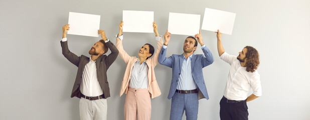 Team of positive people with paper banners sharing message or expressing opinion. Group of four happy male and female business colleagues holding mockup signs standing on light grey studio background