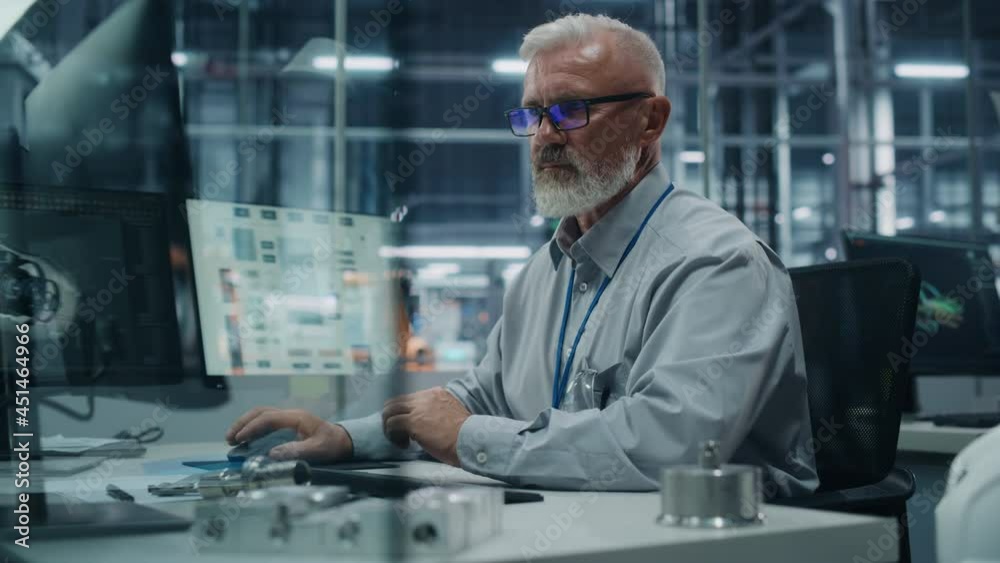 Car Factory Office: Portrait of White Male Chief Engineer Working on Desktop Computer in Automated Robot Arm Assembly Line Manufacturing High-Tech Electric Vehicles. Electronics Production Conveyor Car Factory Office: Portrait of White Male Chief Engineer Working on Desktop Computer in Automated Robot Arm Assembly Line Manufacturing High-Tech Electric Vehicles. Electronics Production Conveyor