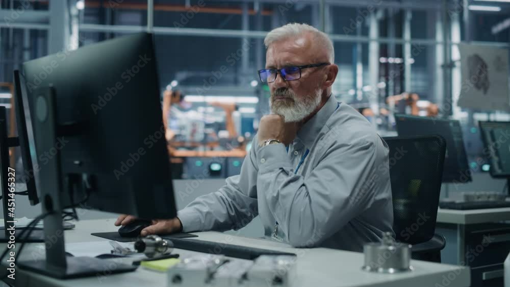 Car Factory Office: Portrait of Senior Male Chief Engineer Working on Desktop Computer in Automated Robot Arm Assembly Line Manufacturing High-Tech Electric Vehicles. Electronics Production Conveyor Car Factory Office: Portrait of Senior Male Chief Engineer Working on Desktop Computer in Automated Robot Arm Assembly Line Manufacturing High-Tech Electric Vehicles. Electronics Production Conveyor